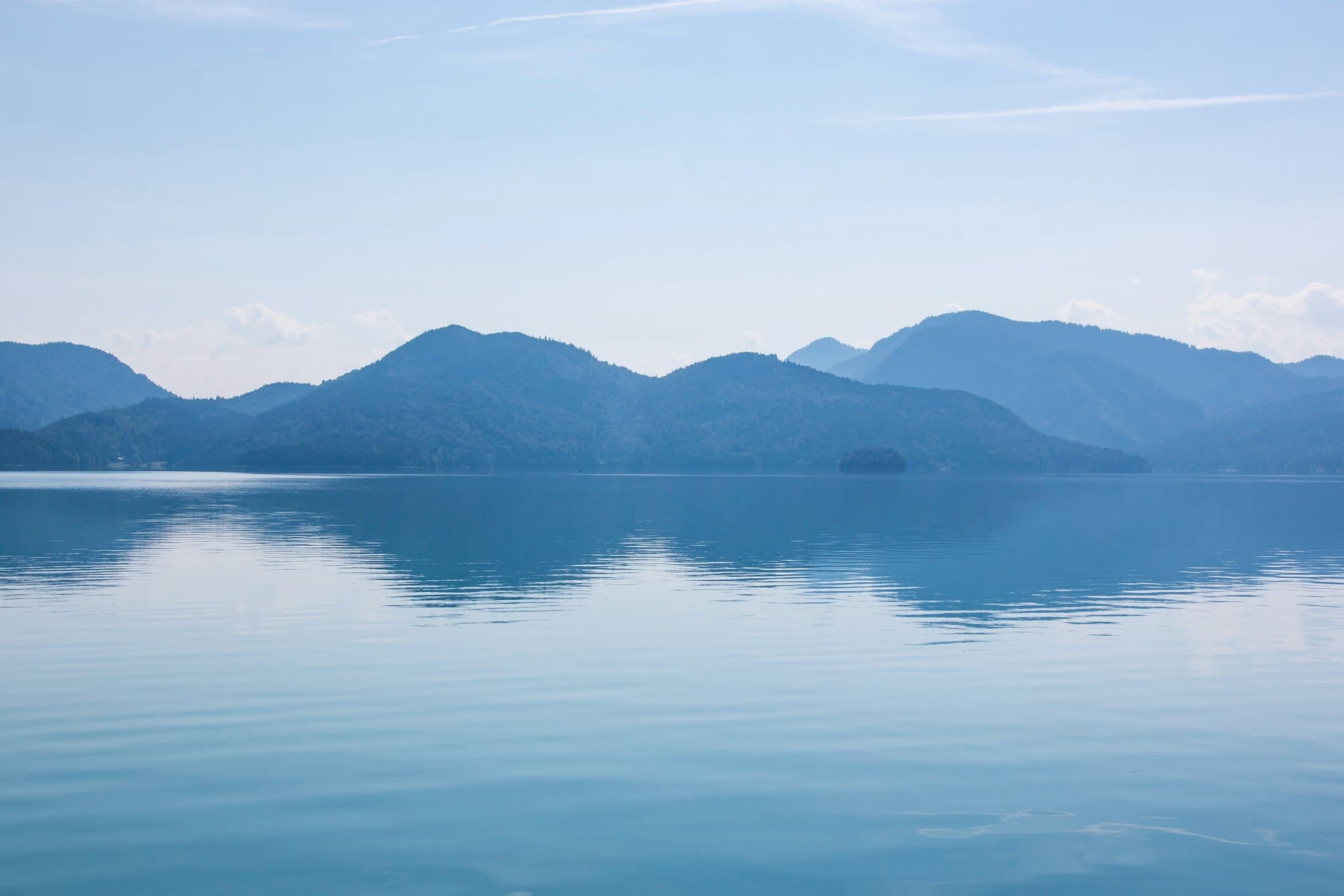 A calm lake reflecting blue mountains